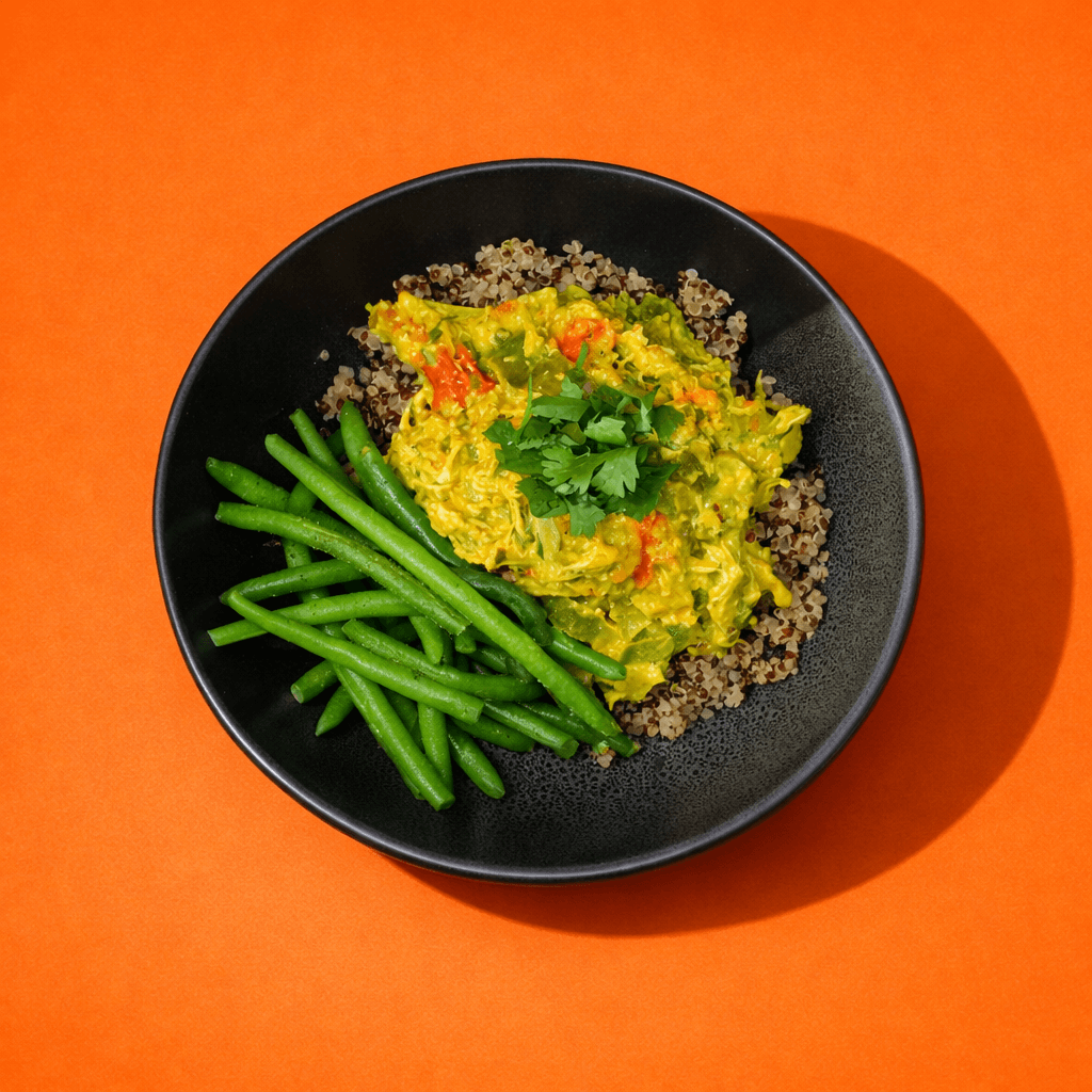 Bol de quinoa avec poulet effiloché au cari coco et haricots verts, repas prêt à manger BigMig sur fond orange.